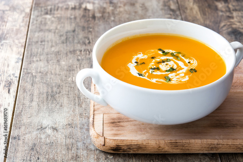 Pumpkin soup in white bowl on wooden table 