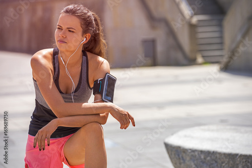 Portrait of young woman look side, standing outdoors with earphones. Female runner relaxing after workout.