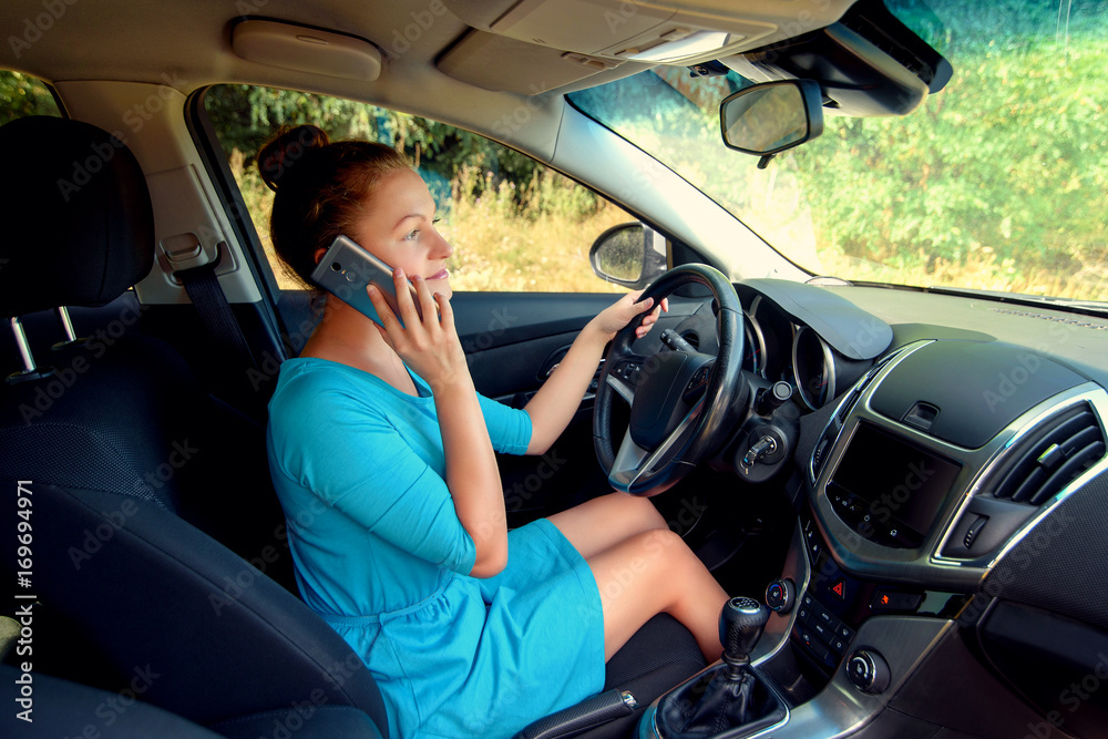 Side view of beautiful young woman driving a car and talking on smart phone, free space. Business woman sitting in car with cell phone,  looking on road