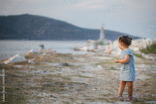 A little girl on a seaside looking back at the sea and lighthouse