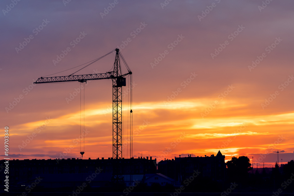 Industrial construction cranes and building silhouettes over sun at sunrise. Background with copy space area for a text.