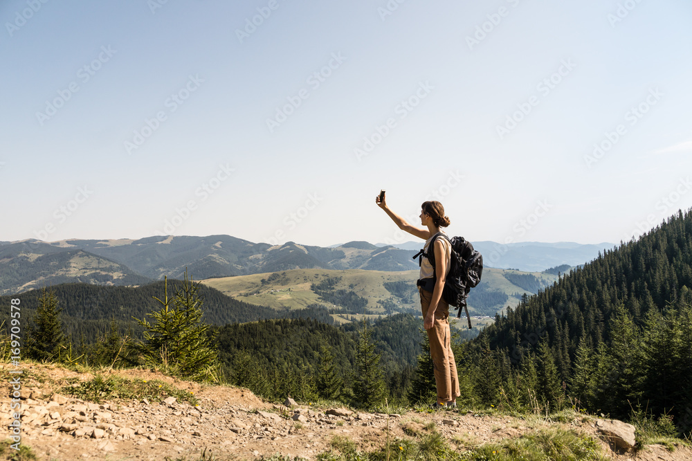 Young female backpacker uses mobile phone for self portrait in rural mountain area of ukrainian carpathian mountains. Girl with tourist rucksack on a long hiking walk looking for network connection Young female backpacker uses mobile phone for self portrait in rural mountain area of ukrainian carpathian mountains. Girl with tourist rucksack on a long hiking walk looking for network connection