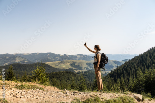 Foto Young female backpacker uses mobile phone for self portrait in rural mountain area of ukrainian carpathian mountains