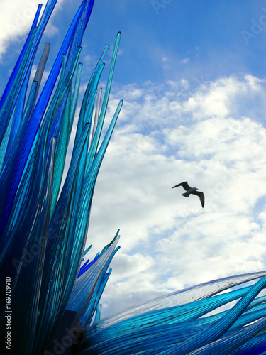 Blue glass sculpture in murano venice with bird flying in summer sky with white clouds