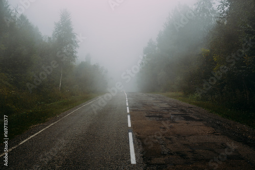 Asphalt road in mountains among green forest in fooggy morning