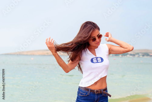 Beautiful young girl with long hair wearing round glasses and a short T-shirt on the beach.