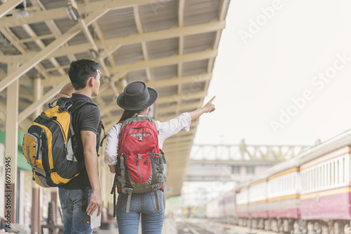 Couple of traveler searching right direction at train station.Asian Backpackers pointing and planning holiday vacation with location map.Travel concept.