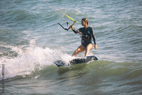 Kite surfing girl in sexy swimsuit with kite in blue sea riding waves with water splash.