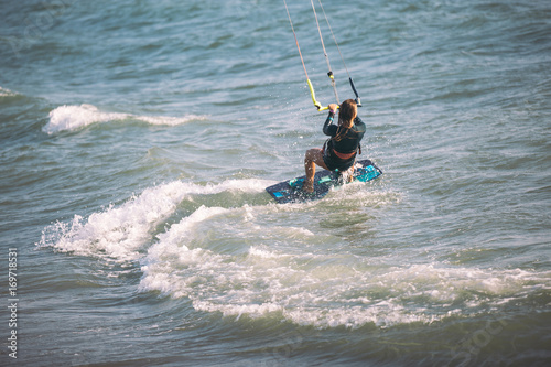 Kite surfing girl in sexy swimsuit with kite in blue sea riding waves with water splash.