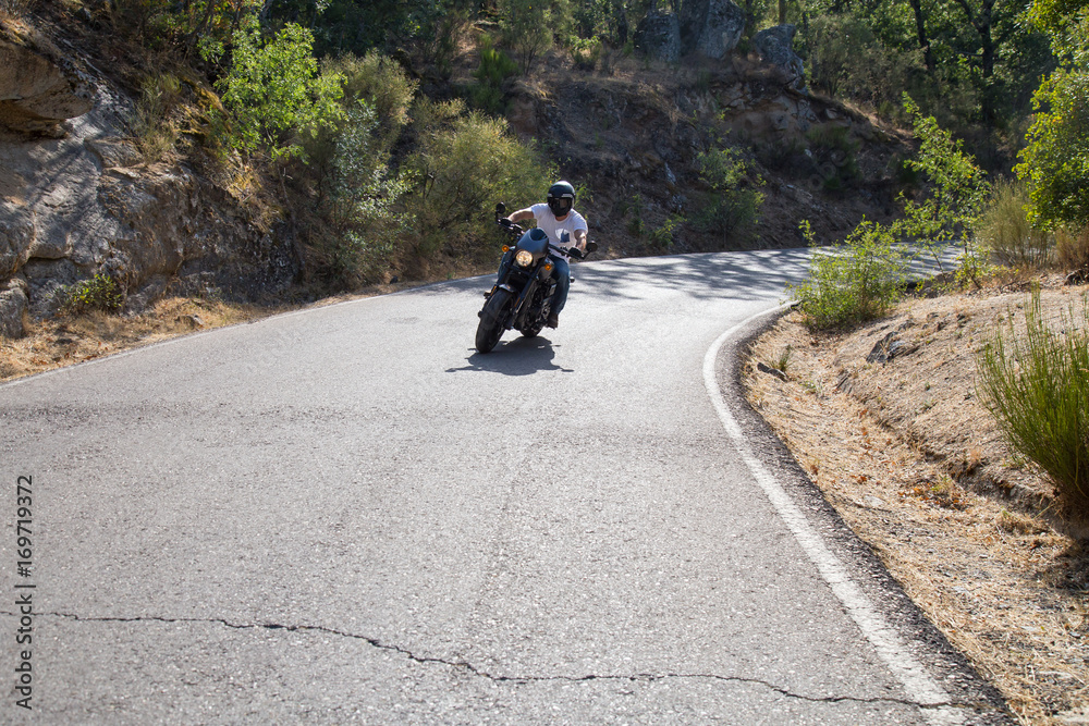 Obraz premium Young man riding a motorcycle on road in bad condition in mountains in sunny day. 