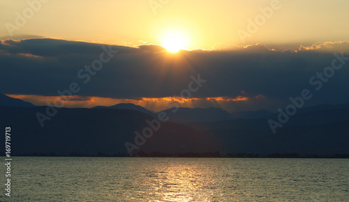 Dramatic sunset sky with dark colored clouds and sun above picturesque calm sea