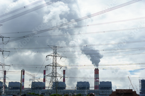 high voltage 500 KV transmission line and pylon with coal fire power plant release steam from stack in the morning background. electricity or climate change concept.