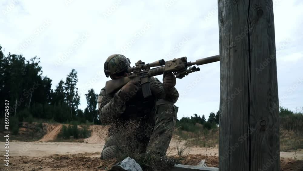 Soldier with a sniper rifle sitting on knee and shooting at terrorist. Military soldier Soldier with a sniper rifle sitting on knee and shooting at terrorist. Military soldier