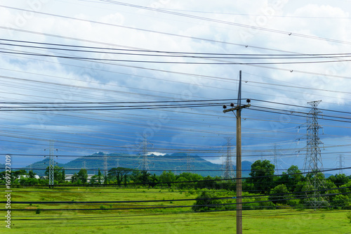 low voltage pole with high voltage electricity pylon and transmission line background in the filed with cloudy sky.