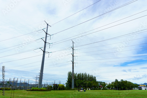 two high voltage electricity pylon and transmission line with power plant background and cloudy blue sky