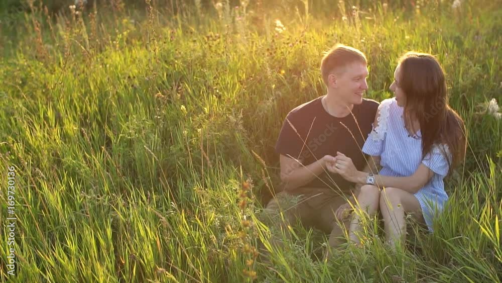 happy couple sitting in a field and watching the sunset happy couple sitting in a field and watching the sunset