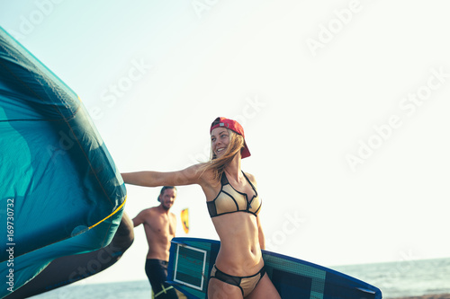 Pretty smiling Caucasian woman kitesurfer walking on the beach with her kite