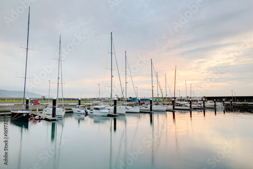 Morning scenery of fishing boats and yachts parking in a marina under cloudy sky with reflections of golden clouds on smooth water, in I-lan, Taiwan