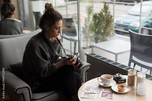 Young woman photographing coffee and photographs on table in