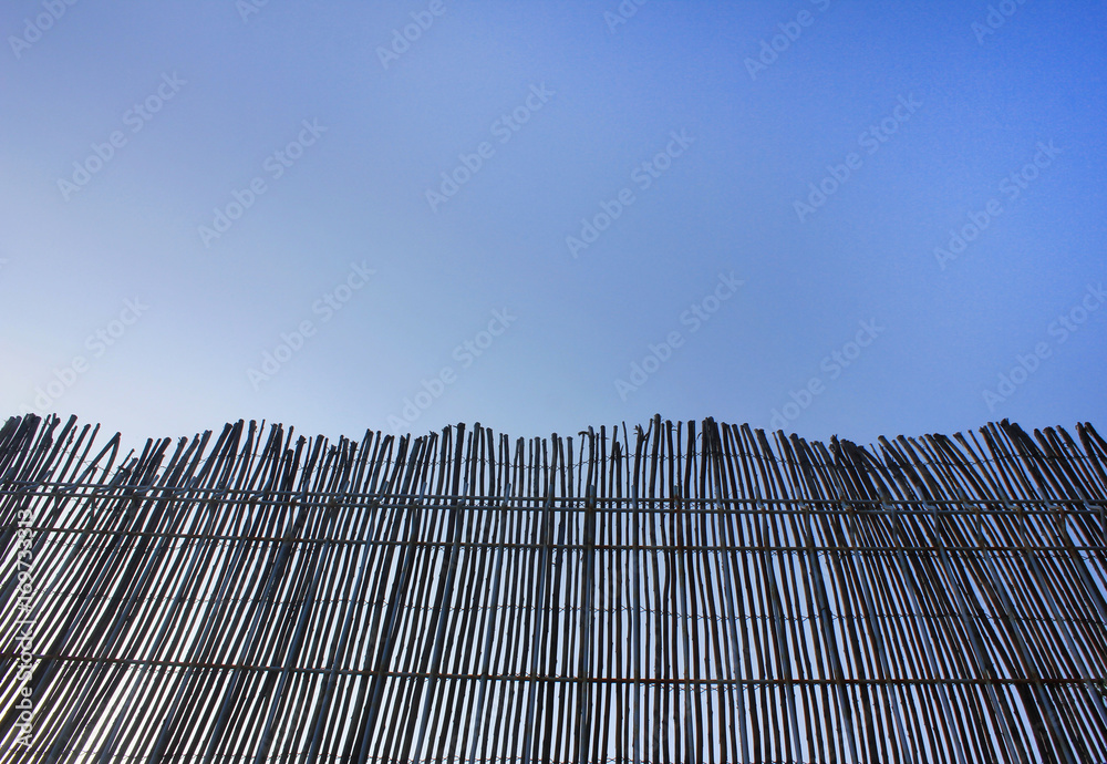 Wooden fence edge against blue clear sky background. Bamboo tree railing barrier helps enclosing an area of ground, mark a boundary, control access, or prevent escape. Empty copyspace low angle view