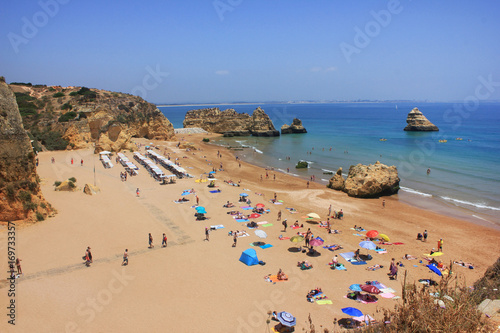Aerial top view Dona Ana Beach in Lagos. Summer scene with local families, young people and tourists relaxing, enjoying swimming in Atlantic ocean on hot day. Algarve region, south Portugal, Europe © onajourney