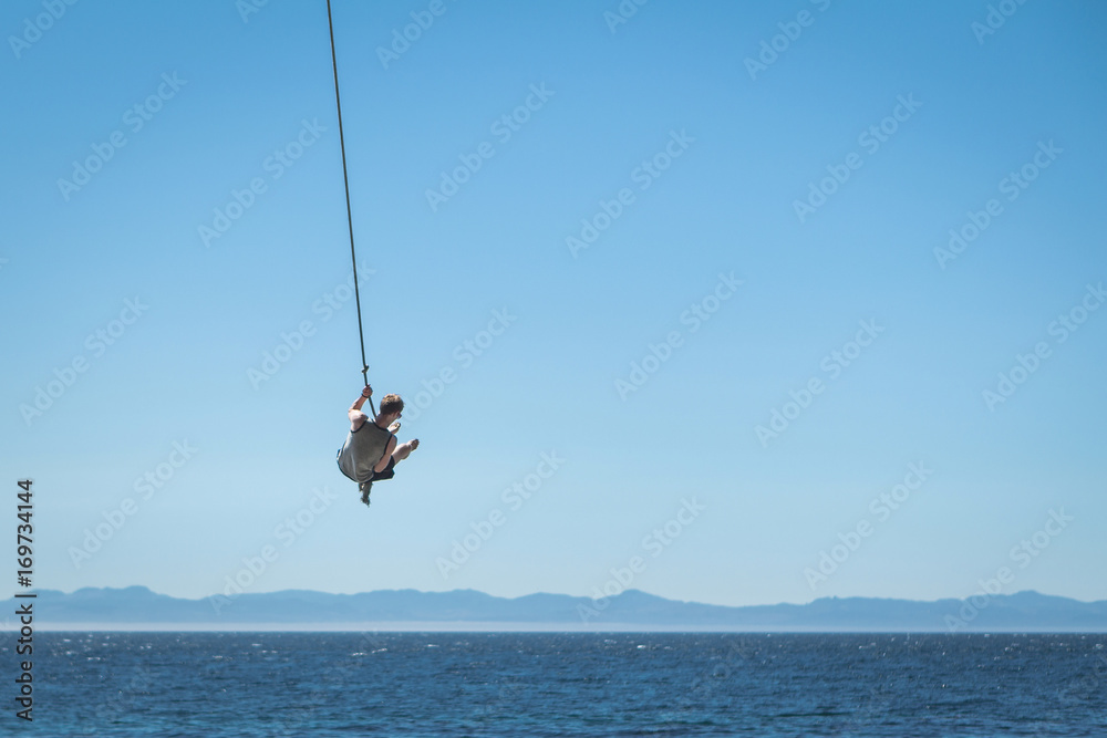 Man swinging on rope over ocean