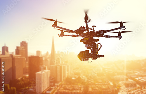 Drone Flying over San-Francisco city. Hexacopter drone with high resolution digital camera on the sky. Heavy lift drone photographing city at sunset. Toned photo with blurred background.
