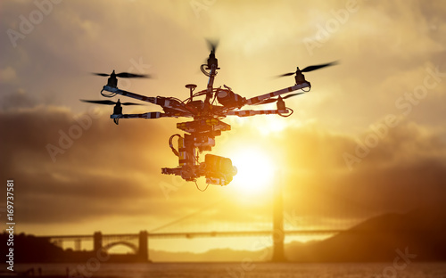 The drone with the professional cinema camera flying over the misty mountains at sunset. Blurred background. Innovation photography concept. Heavy lift drone photographing city at sunset.