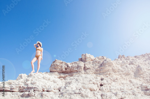 Beautiful girl in a bikini  hat and sunglasses sunbathing on the background of white rocks