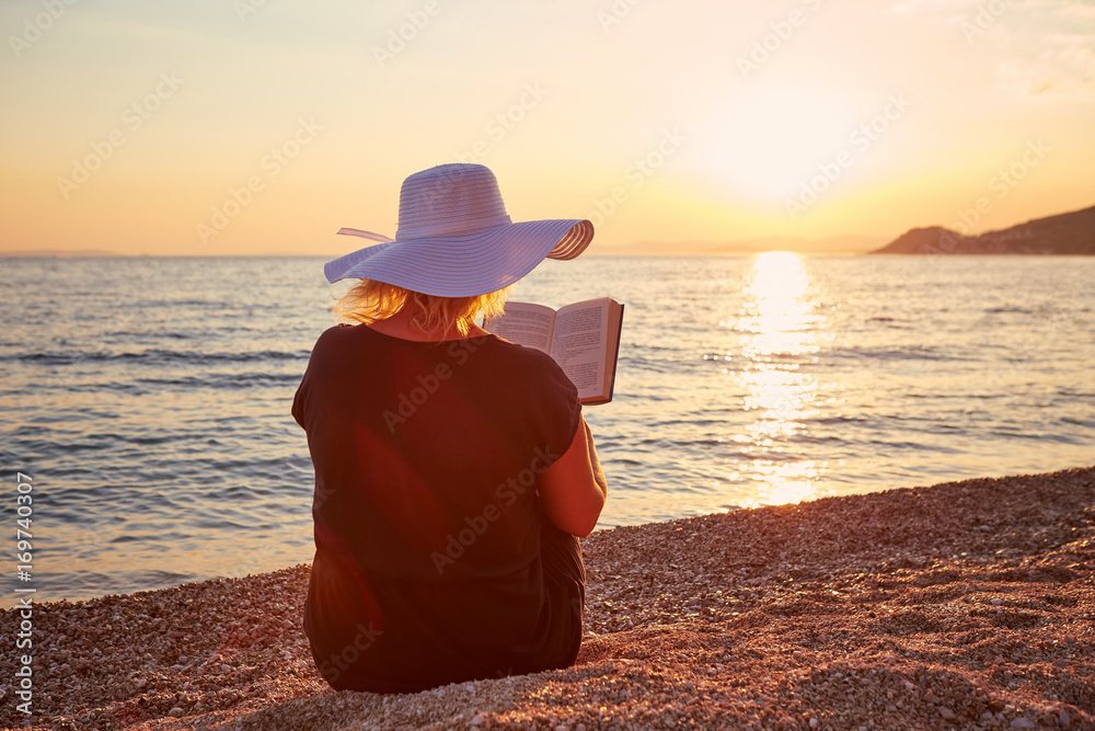 Woman reading a book on the beach at sunset