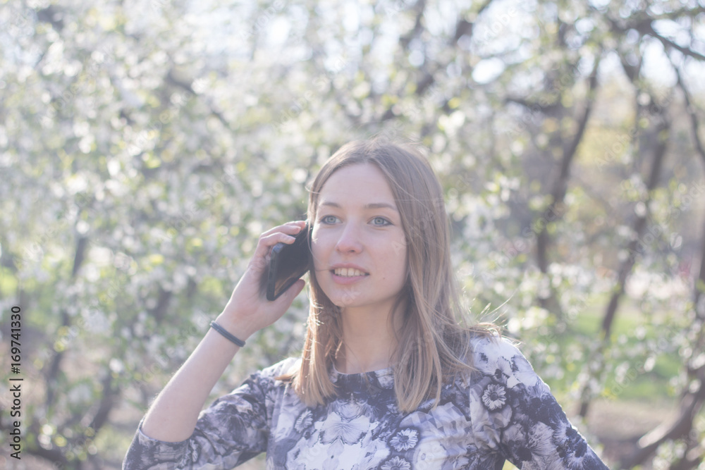 beautiful young womfn in spring park using cellphone and having fun, flower background 