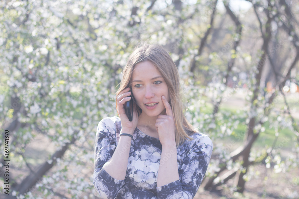 beautiful young womfn in spring park using cellphone and having fun, flower background beautiful young womfn in spring park using cellphone and having fun, flower background