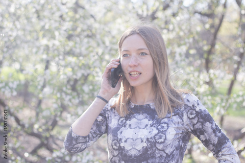 beautiful young womfn in spring park using cellphone and having fun, flower background  © serejkakovalev