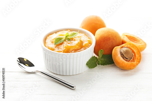 Apricot jam in bowl with spoon on white wooden table