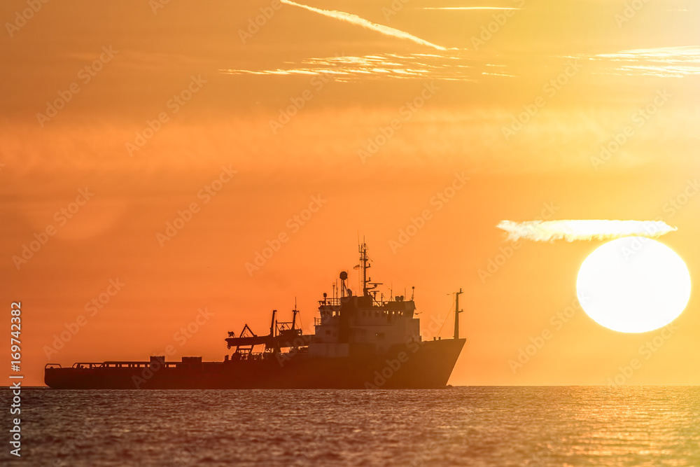 Travel destination. Sun haze over a tropical ocean at sunrise. Fishing boat silhouette infront of a glowing sun.