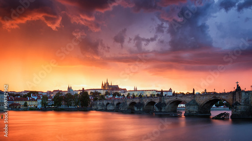 Skyline of Charles bridge and Prague castle on Vltava river during afternoon. Storm clouds with red color. Old Town, Prague, Europe.