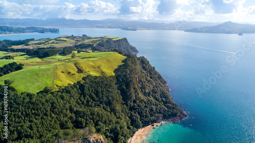 Aerial view on a cliff on a sunny beach with farmland on the background. Coromandel peninsula, New Zealand.