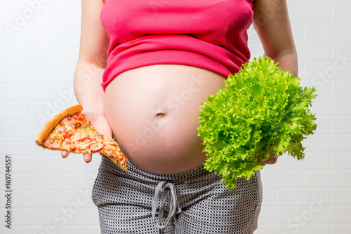 conceptual photo - unhelpful and healthy food in the hands of a pregnant woman on a stomach closeup background photo
