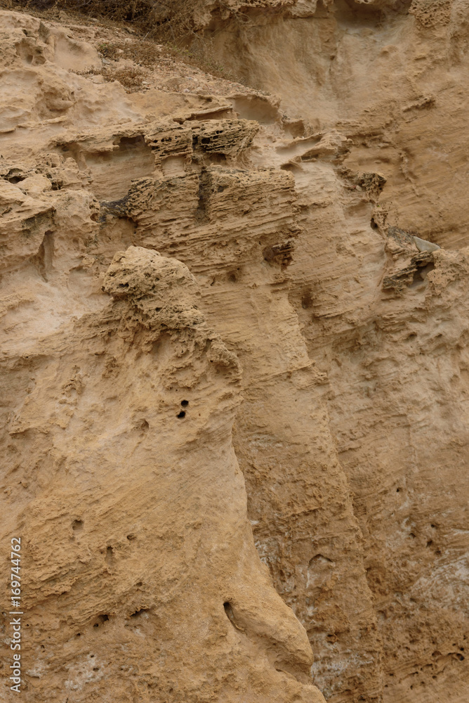 Side view of the natural background of yellow limestone with the bumpy surface with dark hollows that are smoothed by the sea waves 02