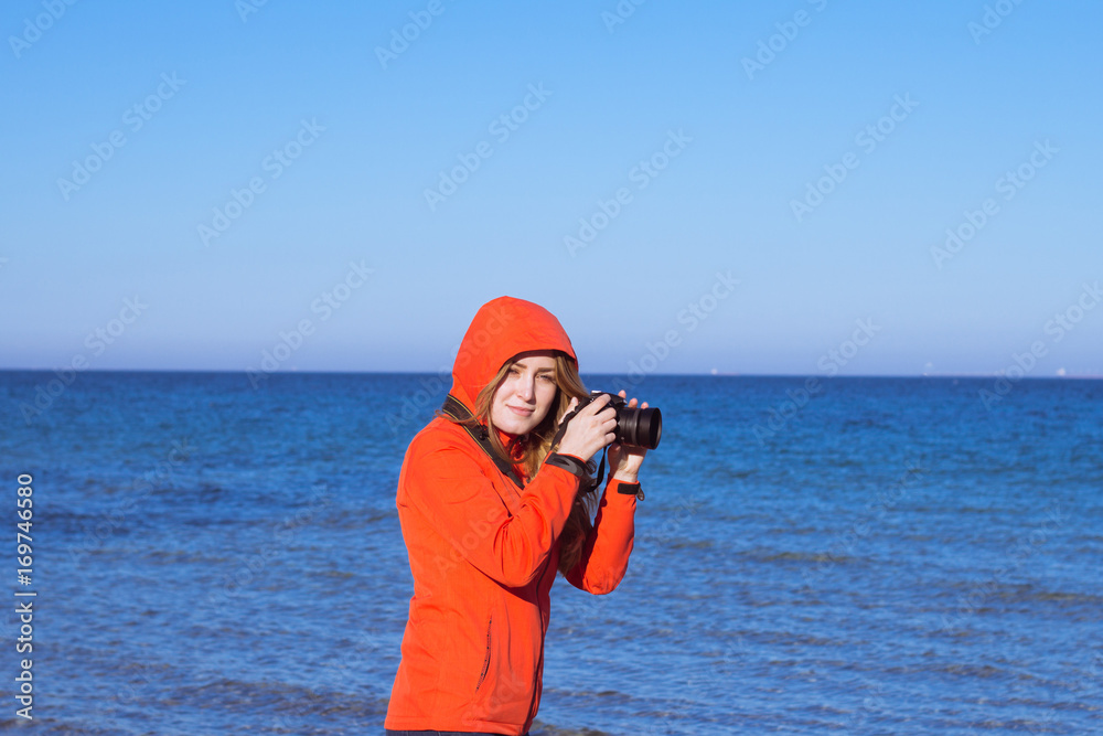 woman tiurist in red jacket with photo camera on the beach, photographer make picture of sea woman tiurist in red jacket with photo camera on the beach, photographer make picture of sea