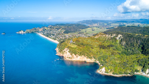 Aerial view on a coastal park area with cliff and forest and residential suburbs on the background. Coromandel, New Zealand.