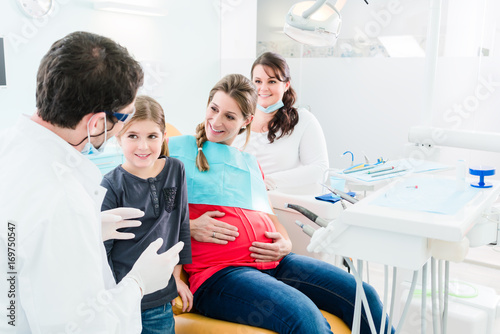 Dentist and his assistant with pregnant woman and child in surgery