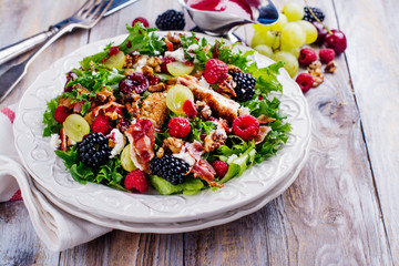 Delicious summer salad with mix of berries, nuts, feta chees, bacon and raspberry sauce on vintage background. Space for text