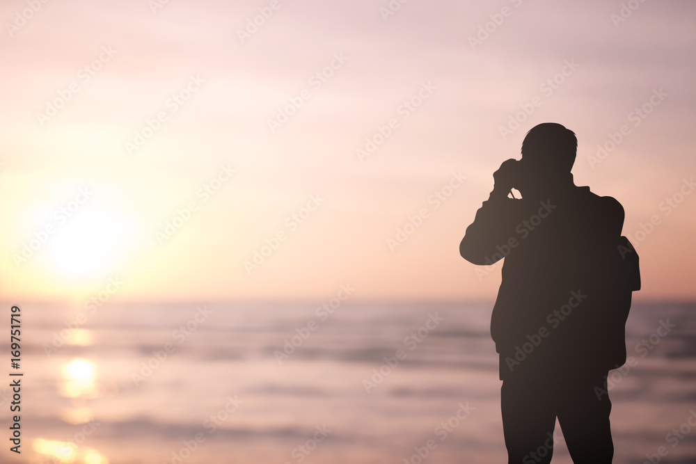 Silhouette traveler man holding camera for take a photo at beach ocean at sunset time background
