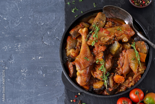 Chicken stewed with vegetables and tomato on a stone board in a frying pan. photo