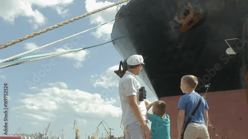 Marine family on the seaport. Captain father and his sons walking at the marina dock together. The man shows the boys the big ship. People engoy seaview on the waterfront photo