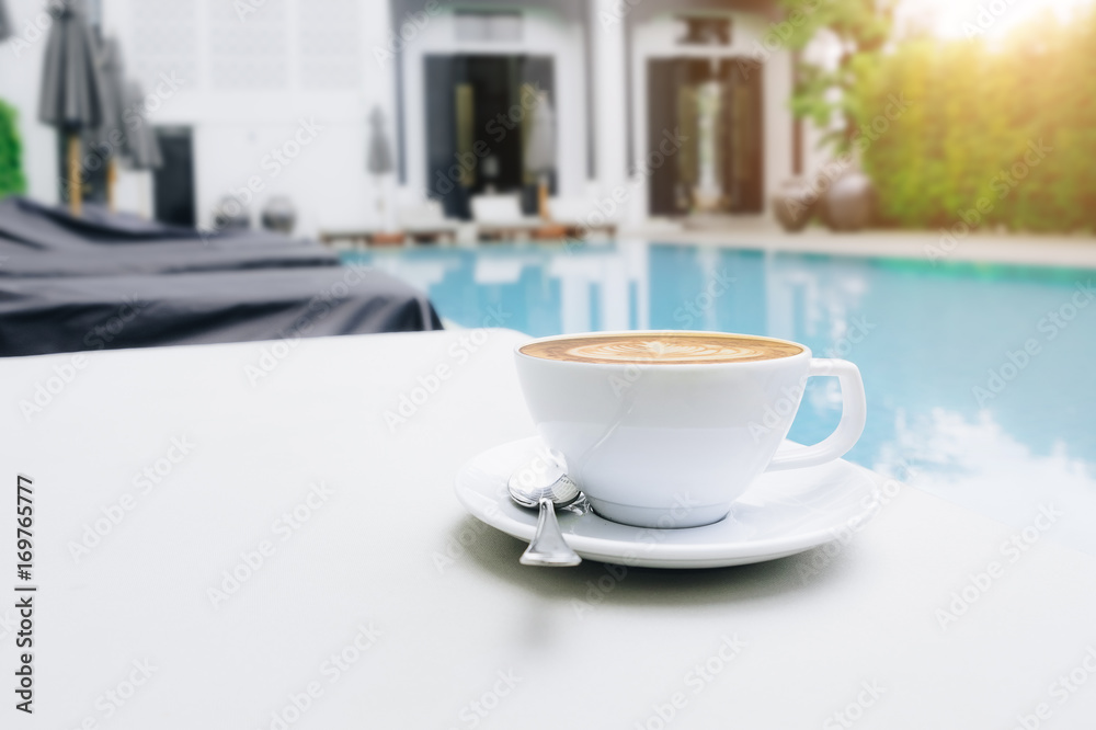 Hot coffee and latte art at the poolside bed with morning light. selective focus.