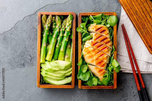 Healthy lunch in wooden japanese bento box. Balanced healthy food grilled chucken and avocado with asparagus and green salad. Top view, slate gray background photo