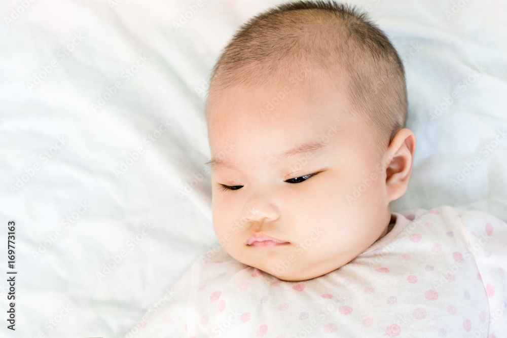 Portrait of adorable baby girl lying on back on the bed and looking in camera indoors Portrait of adorable baby girl lying on back on the bed and looking in camera indoors