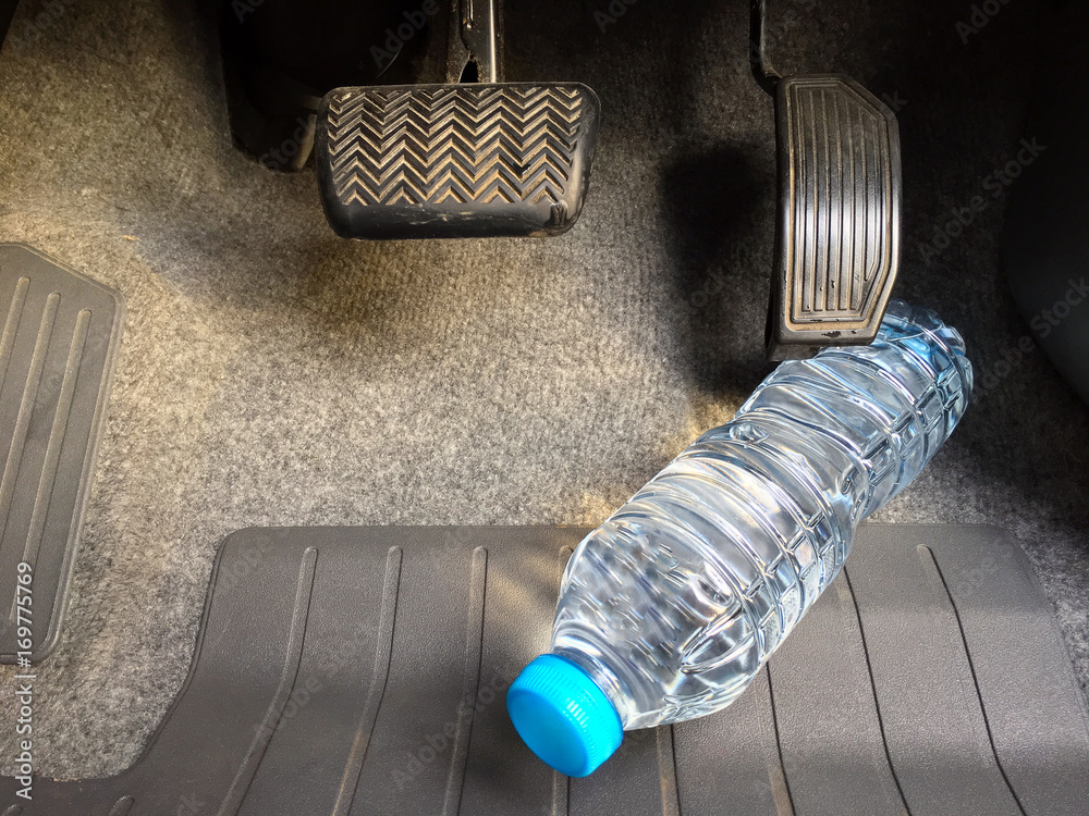 Water bottle getting stuck in the car accelerator and brake peddle  demonstrating the danger of the inability to apply the brake or  acceleration Stock Photo